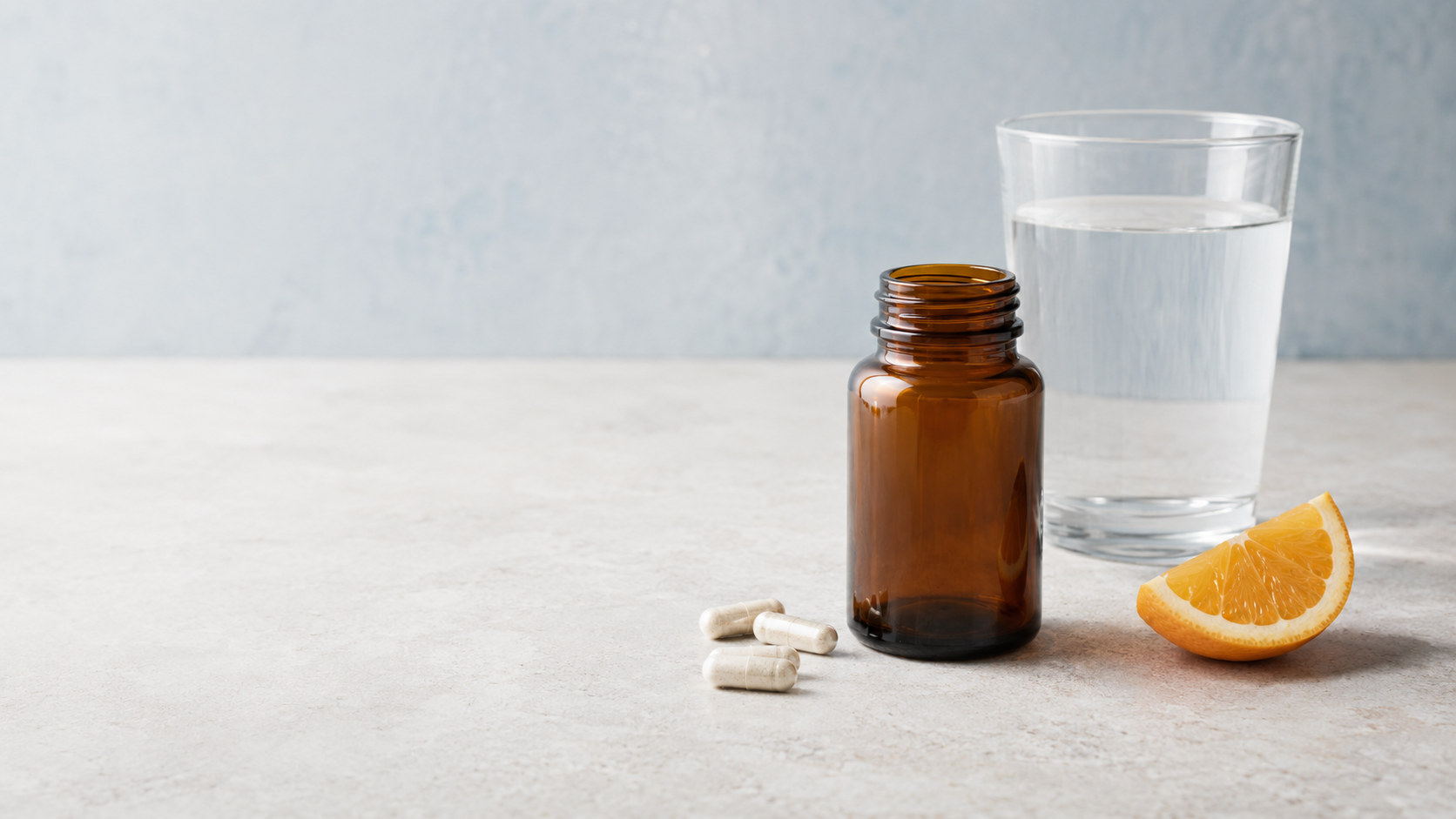Frasco farmacêutico sem rótulo, cápsulas, copo de água e uma fatia de laranja em composição editorial